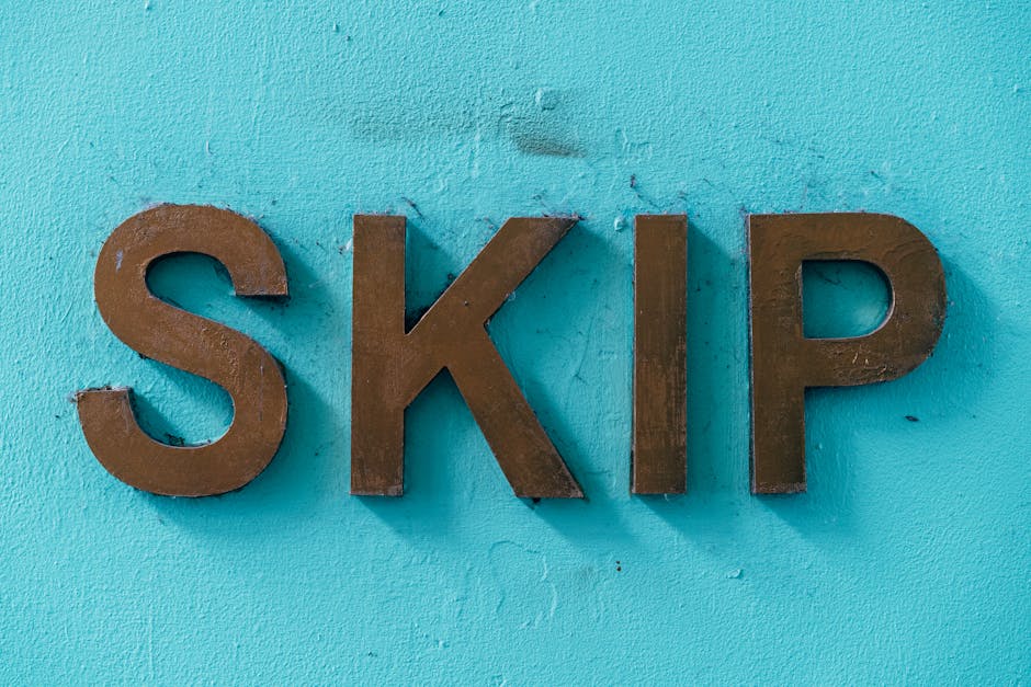 Close-up image of three three-dimensional letters spelling 'SKIP', mounted on a textured light blue wall. The letters are made of dark metal with a matte finish, exhibiting slight wear and patina, pos